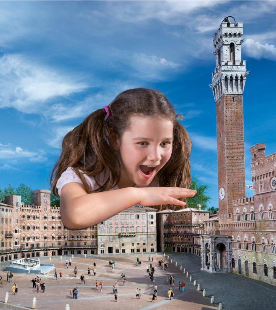 Bambina gigante gioca con entusiasmo sopra una piazza storica in miniatura.