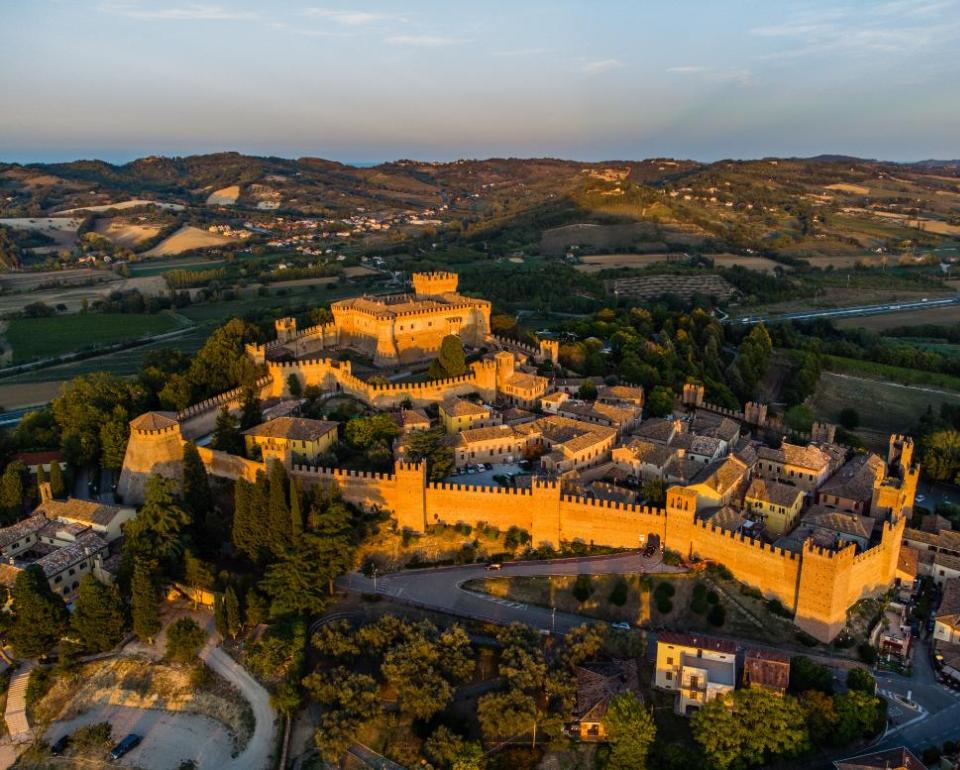 Vista aerea di un castello medievale al tramonto, immerso in colline verdi e dorate.